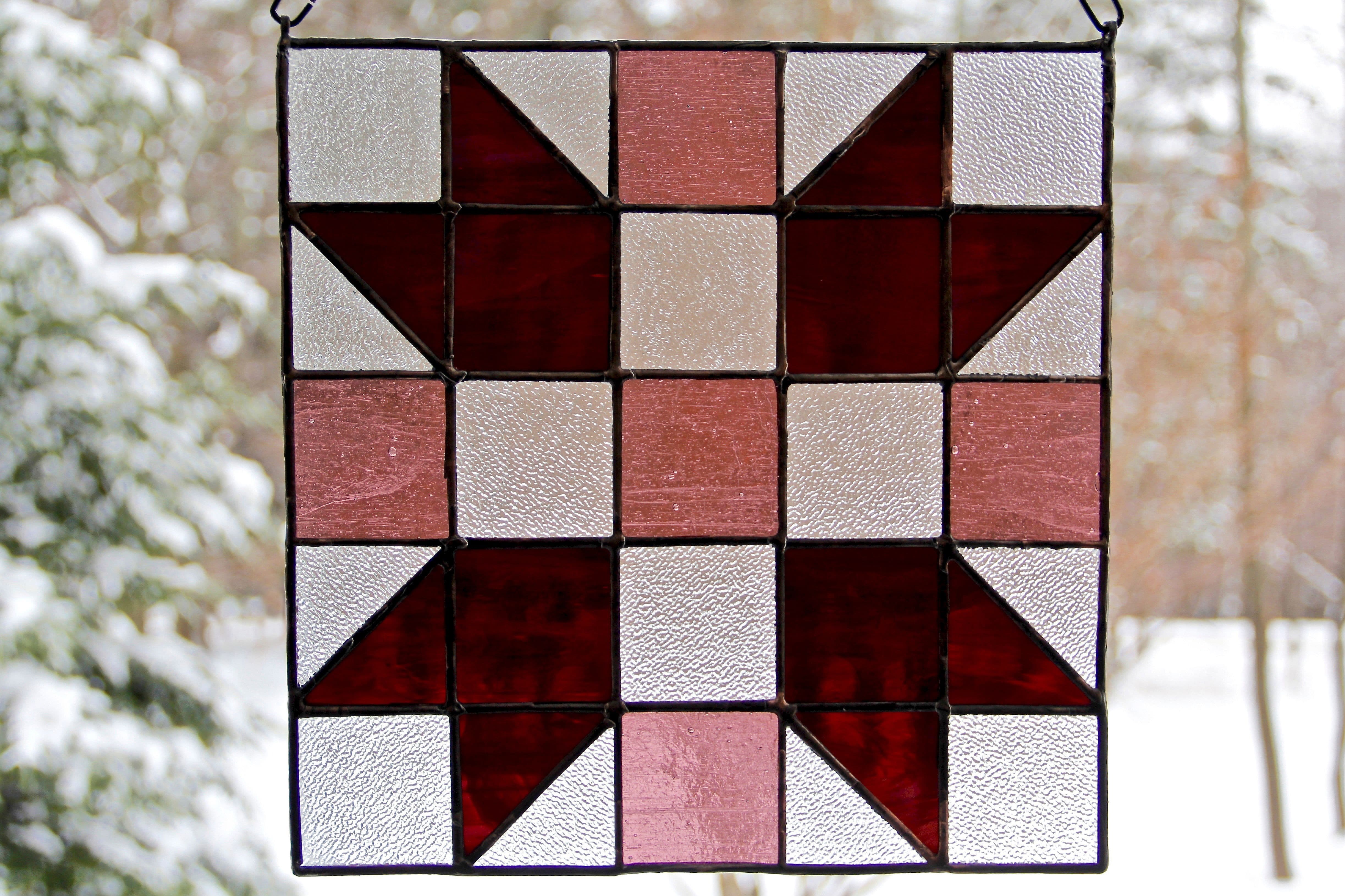 Stained glass rendition of "Sisters," a single block quilt pattern, in purple, against snowy wooded scenery.